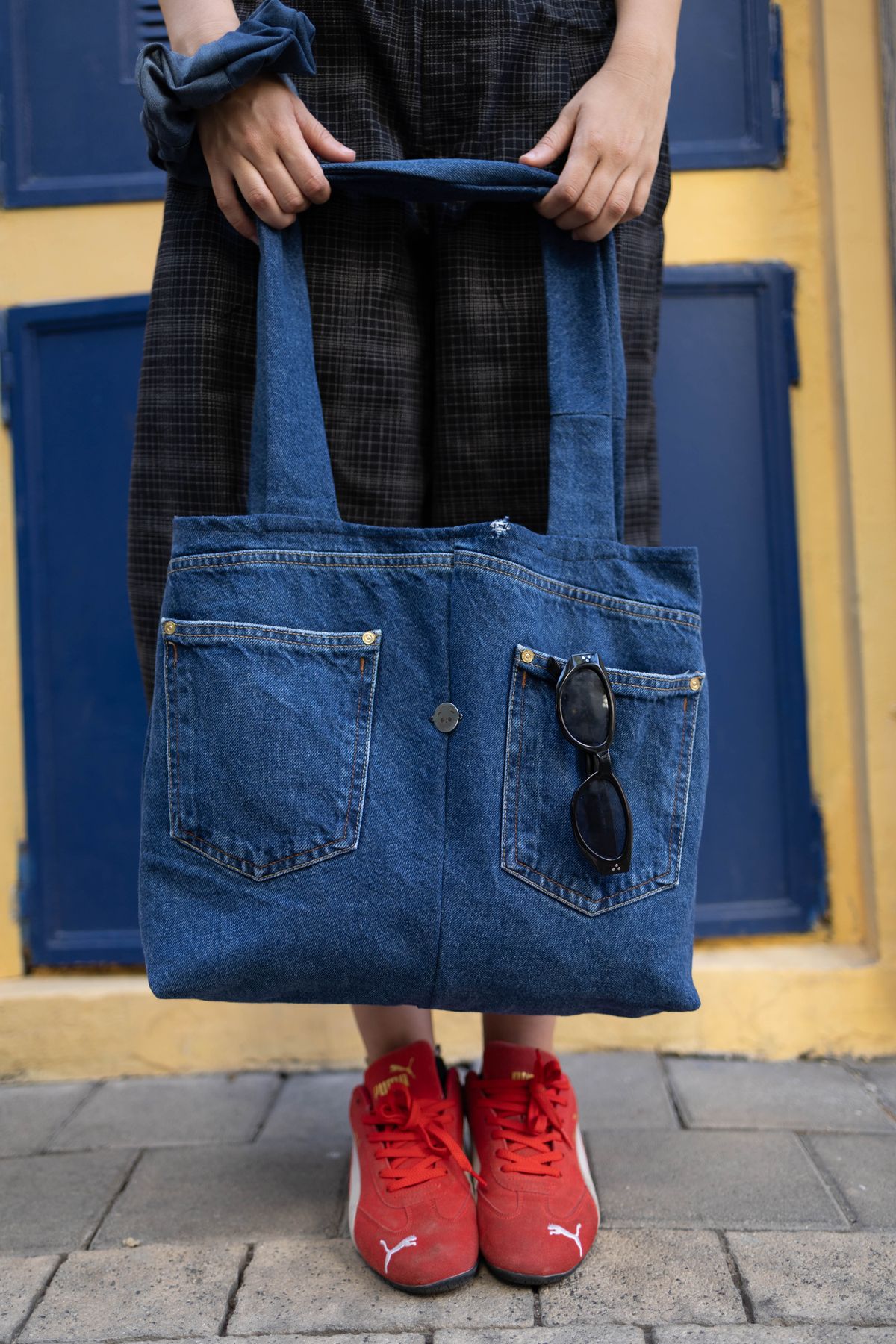 Loop Tote מג'ינס עם כיסים, מוחזק מול תריסים כחולים וקיר צהוב
